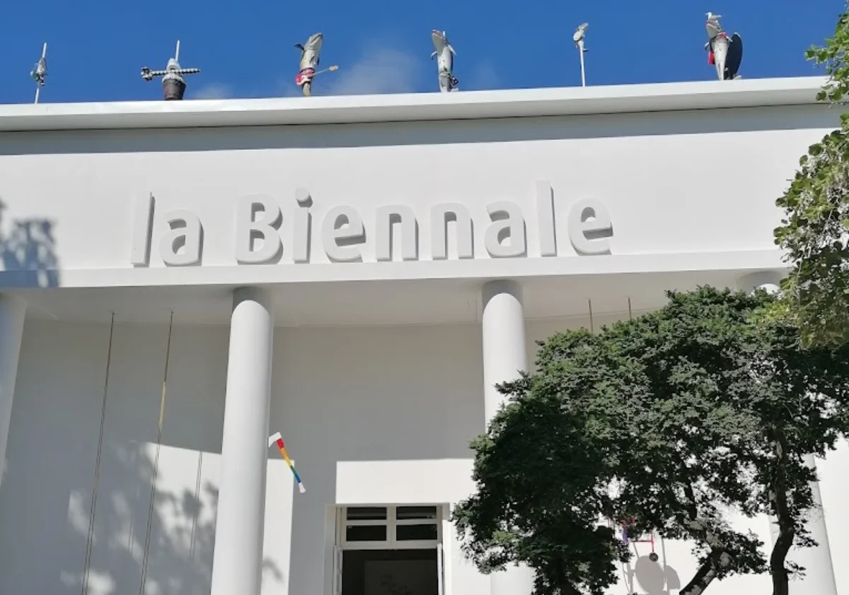 Entrance of La Biennale with artistic mannequins on the roof, against a clear blue sky.