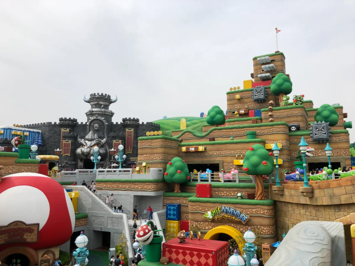 Colourful themed amusement park section inspired by a video game, featuring large iconic green pipes and character statues.