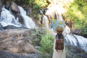 A person wearing a hat and backpack standing in front of a waterfall, looking at a map.