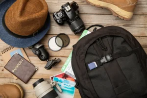 Travel essentials on a wooden surface, including a camera, backpack, hats, boots, and a passport.